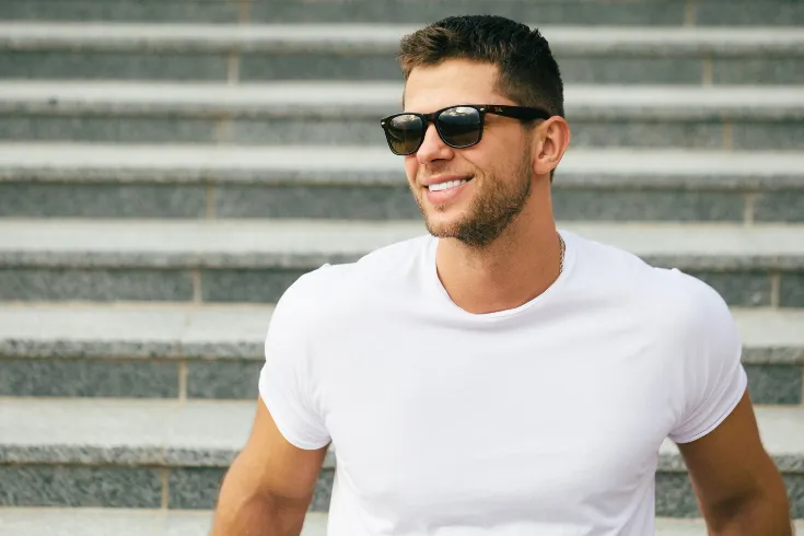 Rapaz de camiseta branca e óculos sorrindo.