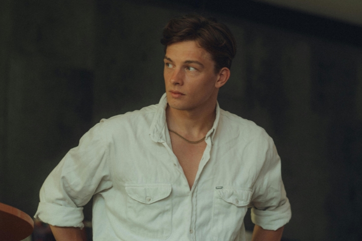 Rapaz de camisa branca, levemente desabotoada, olhando para o lado