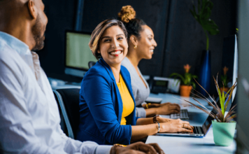 Quais os melhores amuletos contra inveja no trabalho? amuletos contra inveja no trabalho mulher sorrindo no escritório