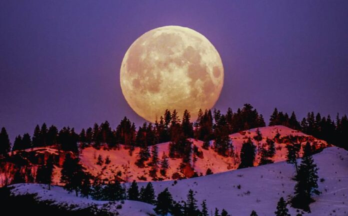 Super lua sob uma montanha em frente a um céu arroxeado