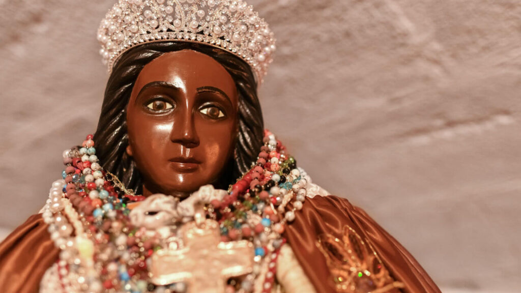 Imagem de uma estatueta da Santa Sara Kali coroada e envolta de terços