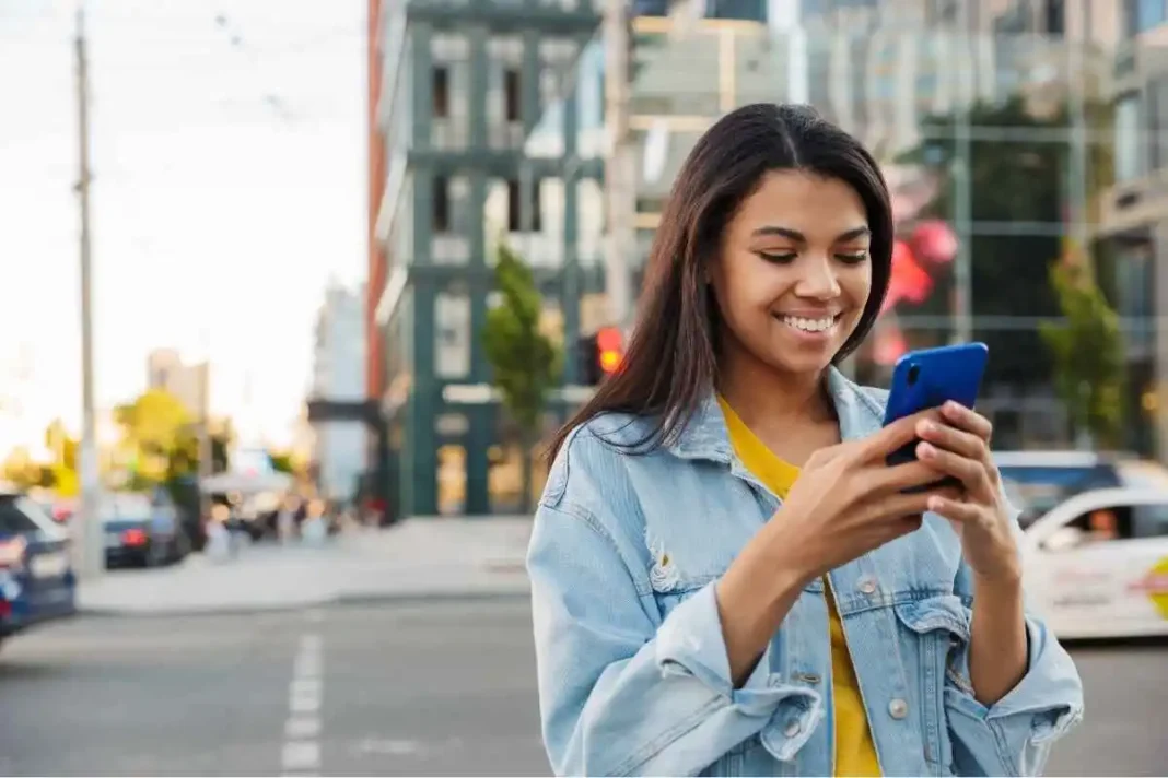 Mulher sorridente, falando com Taróloga ao celular, via chat, enquanto anda pela rua.