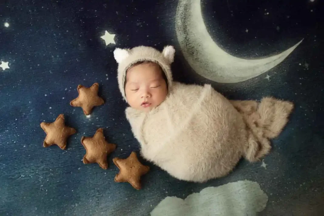 Uma imagem produzida. Bebê, vestido como uma ovelhinha, dormindo sobre "céu noturno" de tecido, com lua e estrelas.
