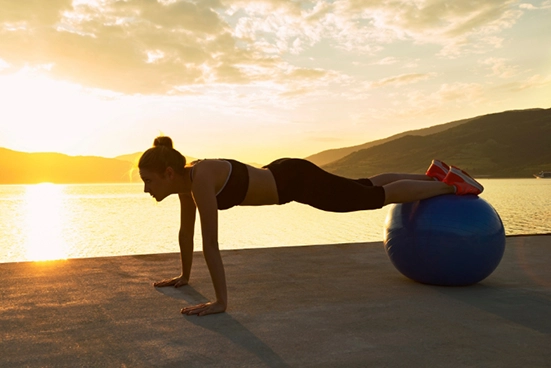 Mulher praticando pilates com bola, em um lindo lago, ao entardecer.