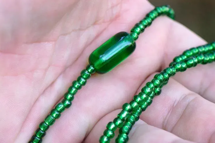 Mão segurando uma guia verde, de Oxóssi