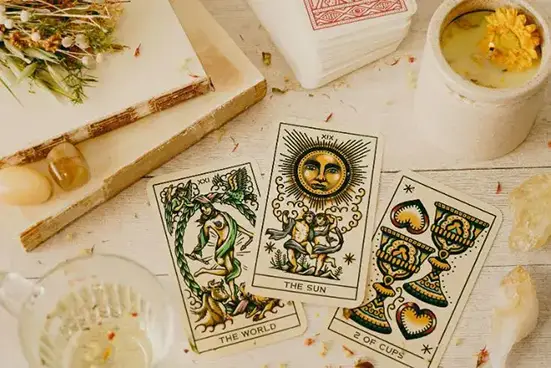 Mesa com três cartas de Tarot dispostas: o Mundo, o Sol, Dois de Copas.