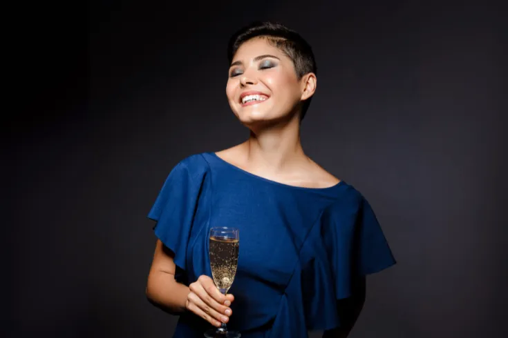 Mulher vestida de azul, segurando taça de champanhe em fundo escuro